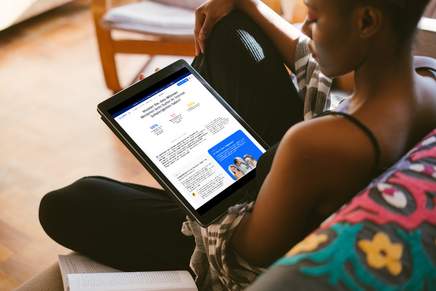 AccessiWay - Digitale Barrierefreiheit Eine dunkelhäutige Frau schaut auf ihren Laptop und sitzt dabei gemütlich auf einer Couch.